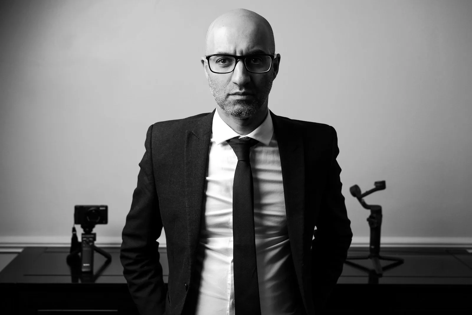 A man in a suit stands in front of camera equipment